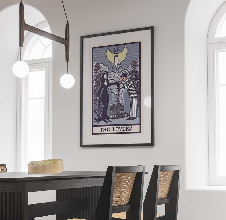 May include: A framed wall art print featuring a tarot card illustration titled THE LOVERS. The artwork depicts a couple in a gothic style, a large house, and a crescent moon with a hand above. The color palette includes shades of purple, black, and cream.