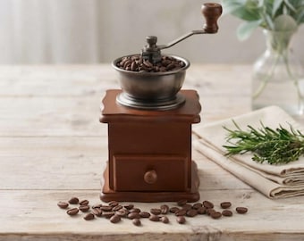 May include: A manual coffee grinder with a dark brown wooden base, a small pull-out drawer with a round knob, and a metallic hopper on top. A dark metal hand crank extends from the hopper. Roasted coffee beans fill the hopper and scatter.