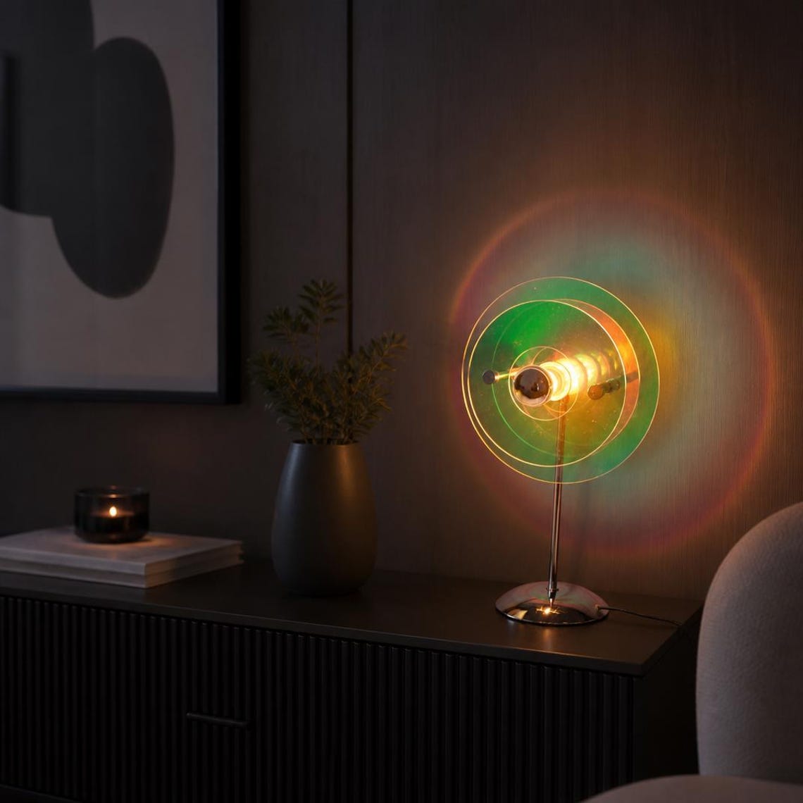 May include: A table lamp featuring a central light bulb surrounded by three concentric, translucent, iridescent circular acrylic discs. The lamp has a thin, silver-toned metal stand and a circular base, emitting a warm glow with green and orange light.
