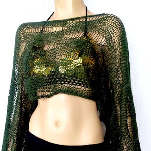 Pode incluir: Um top de manga comprida em tecido aberto verde escuro com um top halter a condizer por baixo. O top é combinado com uma saia preta. A roupa é exibida num manequim.