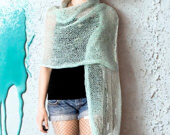 Peut inclure: Un châle vert clair en tricot ajouré drapé sur une personne. Le châle semble léger et vaporeux. La personne porte un haut noir, un short en jean, des bas résille et des jambières. La couleur du châle est un vert pastel.