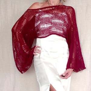 May include: A burgundy, open-weave, off-the-shoulder top with long, bell sleeves. The top is paired with a white, satin, floor-length skirt. The top's texture and color create a striking contrast with the skirt's smooth, bright surface.