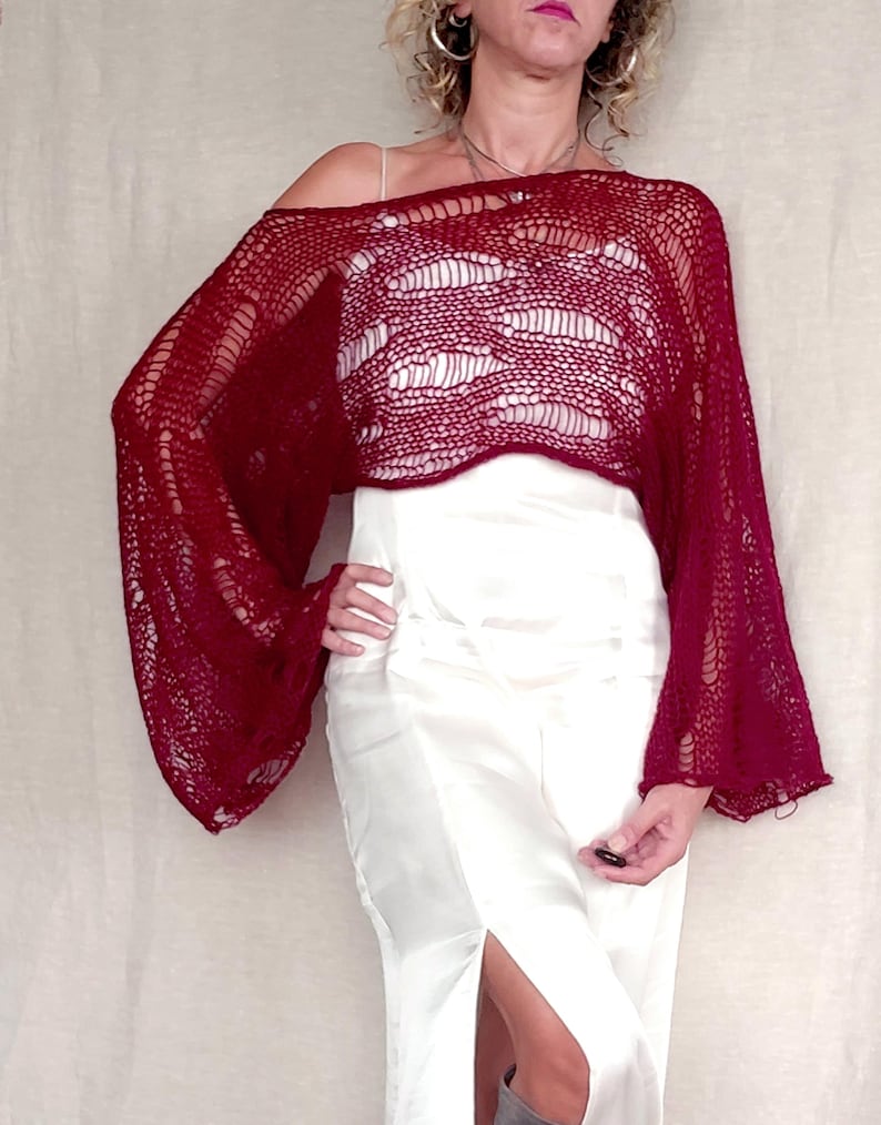 May include: A burgundy, open-weave, off-the-shoulder top with long, bell sleeves. The top is paired with a white, satin, floor-length skirt. The top's texture and color create a striking contrast with the skirt's smooth, bright surface.