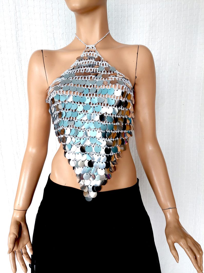 This silver halter top is hand-crocheted with oversized mirror sequins that shimmer and move with light. The shape flatters with a pointed front and tie-up neck, ideal for styling with skirts or wide-leg pants for a festival, club, or New Year’s Eve look.