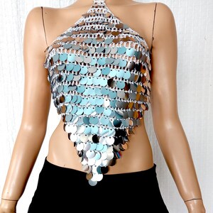 Sparkling silver crochet halter top featuring layers of mirrored sequin discs that create a fish-scale texture. The V-cut design flatters the waistline, and the shimmering finish makes it a standout piece for events, costumes, or nightlife outfits.