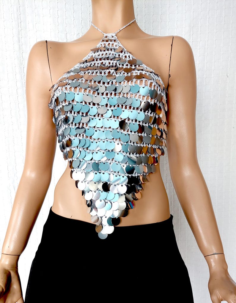 Sparkling silver crochet halter top featuring layers of mirrored sequin discs that create a fish-scale texture. The V-cut design flatters the waistline, and the shimmering finish makes it a standout piece for events, costumes, or nightlife outfits.