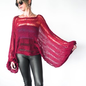A red, open-weave knit sweater with wide bell sleeves. The sweater has a square neckline and a gradient color effect, transitioning from a deep red to a lighter shade. The sleeves are long and flared, creating a dramatic silhouette.