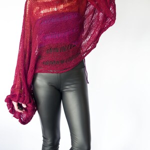 A burgundy open-knit sweater with long sleeves and a wide neckline. The sweater is paired with black faux leather leggings. The top has a gradient effect, transitioning from red to a darker shade.