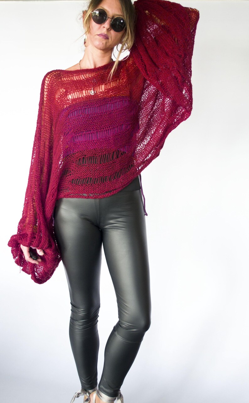 A burgundy open-knit sweater with long sleeves and a wide neckline. The sweater is paired with black faux leather leggings. The top has a gradient effect, transitioning from red to a darker shade.