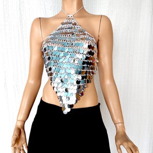 A dazzling silver halter top handmade with shimmering reflective sequins, arranged in a V-shaped silhouette. The top features an open crochet base with light-catching metallic discs, perfect for festival wear, club nights, or statement outfits.