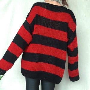 May include: Red and black striped knitted sweater with a loose fit and long sleeves.