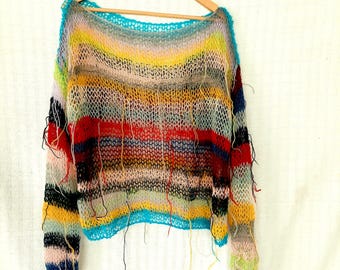 May include: A colorful, open-weave sweater with a scoop neck, hanging on a wooden hanger. The sweater features horizontal stripes in various colors, including blue, yellow, red, and black. Loose threads hang from the bottom and sleeves, adding to the unique design.