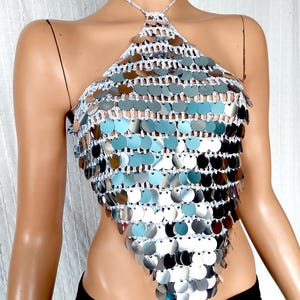May include: A silver halter top with a crocheted design and silver sequins. The top is sleeveless and has a halter neck.