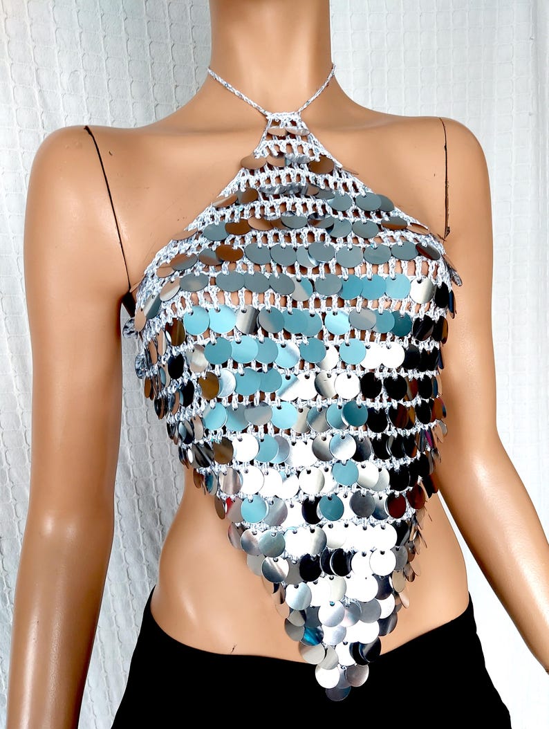 May include: A silver halter top with a crocheted design and silver sequins. The top is sleeveless and has a halter neck.