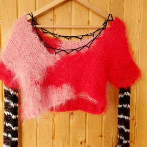 Puede incluir: Un top corto de punto rosa y rojo con detalles de crochet negro y mangas a rayas.