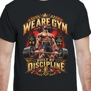 Könnte beinhalten: Ein schwarzes Kurzarm-T-Shirt mit einem Grafikdruck einer muskulösen Figur, die eine Langhantel hebt. Der Text lautet WE ARE GYM und BUILT BY DISCIPLINE in goldener Schrift, ergänzt durch ein Kronensymbol über der zentralen Figur.