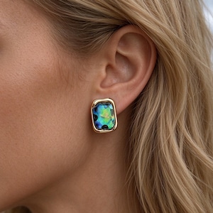 May include: A rectangular stud earring featuring a polished gold-tone metal frame surrounding a vibrant, iridescent abalone shell inlay with swirling blue, green, and purple tones, secured to the earlobe with a simple post backing.