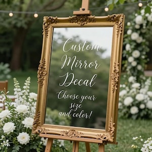 May include: A rectangular mirror with an ornate, vintage-style gold frame mounted on a wooden easel. The mirror surface features white cursive text that reads: Custom Mirror Decal, Choose your size and color!