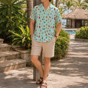 May include: A light blue short-sleeve button-down shirt featuring a repeating pattern of colorful carnival-themed icons including popcorn, balloons, and ribbons, paired with solid beige shorts and brown leather sandals with double straps.