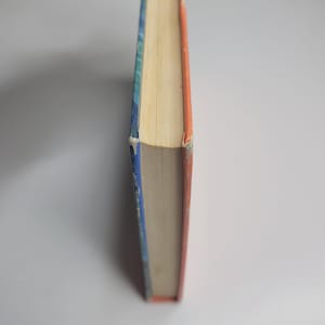 May include: A hardcover book with a blue and orange spine. The pages are yellowed, and the edges of the cover show wear. The book is set against a white background, with the spine facing the viewer.