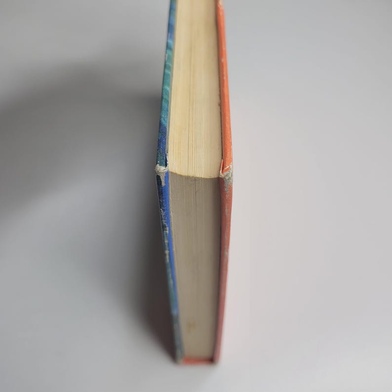 May include: A hardcover book with a blue and orange spine. The pages are yellowed, and the edges of the cover show wear. The book is set against a white background, with the spine facing the viewer.