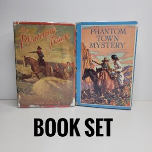 May include: Two hardcover books titled The Phantom Town by Carol Norton and Phantom Town Mystery. Both covers feature illustrations of people riding horses in a desert landscape with rocky terrain, rendered in muted tones of red, blue, and brown.