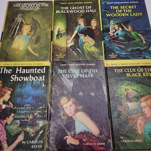 May include: A collection of vintage Nancy Drew mystery books. The covers feature colorful illustrations and titles like "The Secret in the Old Attic," "The Ghost of Blackwood Hall," and "The Haunted Showboat." The books are by Carolyn Keene.