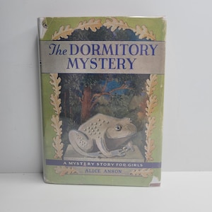 May include: Vintage hardcover book titled "The Dormitory Mystery" by Alice Anson. The cover features a green border with a frog illustration and a forest scene. The text "A Mystery Story for Girls" is also visible.