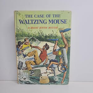 Könnte beinhalten: Vintage-Buch mit dem Titel "The Case of the Waltzing Mouse: A Brains Benton Mystery". Das Cover zeigt eine Illustration eines Bootes mit drei Jungen, von denen einer Kopfhörer trägt, und einen Taucher. Das Buch hat ein grün-weißes Farbschema.