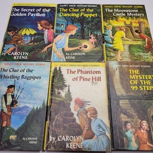 May include: A collection of vintage Nancy Drew mystery books. The covers feature colorful illustrations and titles like "The Secret of the Golden Pavilion" and "The Clue of the Dancing Puppet." The author's name, Carolyn Keene, is printed on each book.