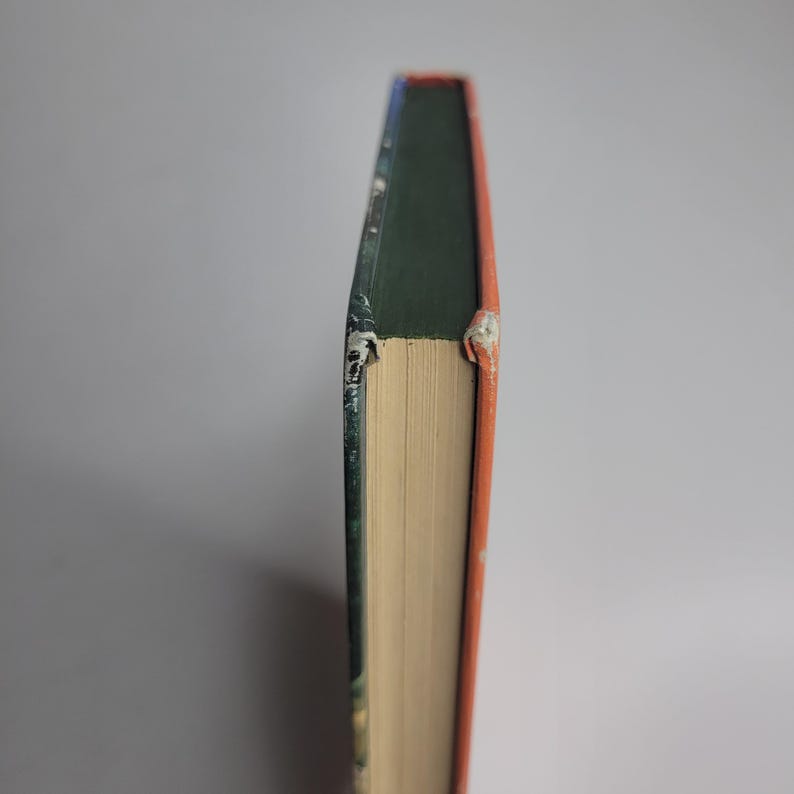 May include: A hardcover book with a green spine, orange edges, and a blue top. The pages are a light beige color. The book shows signs of wear and tear.