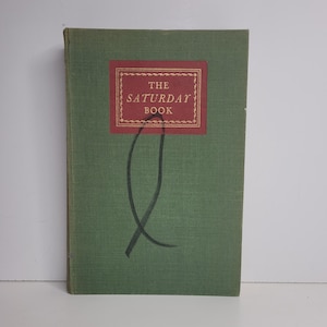 May include: A vintage hardcover book titled "The Saturday Book." The book has a green cover with a rectangular red and gold label. The label features the title in white text. A black, curved design is on the cover.