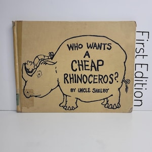 May include: A vintage children's book titled "Who Wants a Cheap Rhinoceros?" by Uncle Shelby. The cover features a black illustration of a rhinoceros with a person riding on its back, and the text is in black. The book is a first edition.