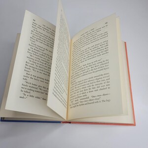 May include: An open book with pages displaying printed text. The book has a blue spine and red and orange edges. The pages are off-white, and the text is black. The book is slightly angled, showing the text and the binding.