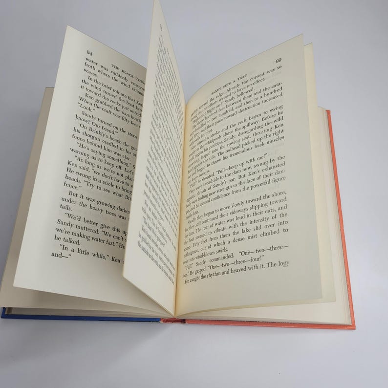May include: An open book with pages displaying printed text. The book has a blue spine and red and orange edges. The pages are off-white, and the text is black. The book is slightly angled, showing the text and the binding.
