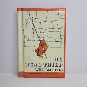 Könnte beinhalten: Ein Hardcover-Buch mit dem Titel "The Real Thief" von William Steig. Das Cover zeigt eine Illustration einer Gans in roter Uniform, die einen Speer hält, vor dem Hintergrund einer Steinmauer. Der Buchrücken ist cremefarben.