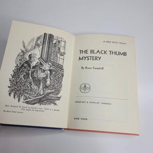 May include: Open book titled "THE BLACK THUMB MYSTERY" by Bruce Campbell. The cover is off-white with black text and a black and white illustration of two men. Published by Grosset & Dunlap, New York.