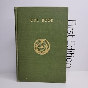 May include: A green hardback book with the title "ODE BOOK" in gold lettering. A gold emblem featuring a five-pointed star and other symbols is centred on the cover.