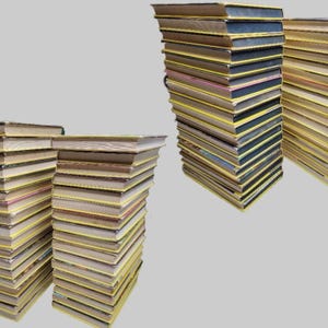 May include: Several stacks of books with yellow spines and varying cover colors are arranged against a gray background. The books appear to be of similar size and thickness, suggesting a collection or series.