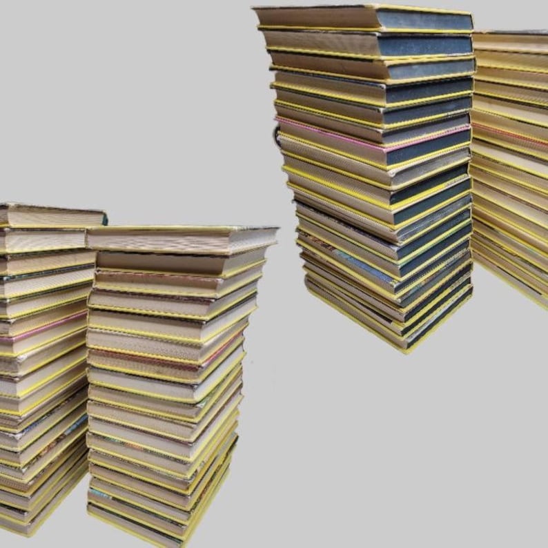 May include: Several stacks of books with yellow spines and varying cover colors are arranged against a gray background. The books appear to be of similar size and thickness, suggesting a collection or series.