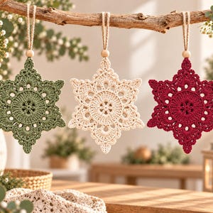 May include: Three star-shaped ornaments crafted from crochet yarn in sage green, cream, and deep red. Each ornament features a central circular pattern with intricate lace-like edges, suspended by a jute twine loop with a small wooden bead.