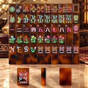 May include: A set of brown tortoiseshell-patterned mahjong tiles featuring colorful engraved designs including numbers, bamboo stalks, Chinese characters, flowers, butterflies, and the word JOKER. The tiles are arranged in a grid.