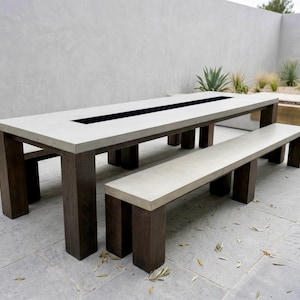 May include: A modern outdoor dining set featuring a long rectangular table with a recessed black center and a matching bench. The table and bench have light gray tops and dark brown legs, creating a minimalist aesthetic.