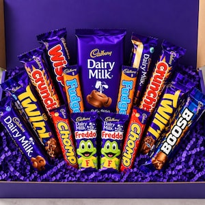 Peut inclure: Une boîte cadeau violette remplie d'un assortiment de barres chocolatées Cadbury, notamment Dairy Milk, Wispa, Crunchie, Twirl, Fudge, Chomp, Freddo et Boost. La boîte contient diverses friandises emballées individuellement sur du papier violet.