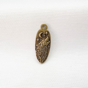May include: An oval-shaped antique brass charm featuring an embossed design of a howling wolf, a crescent moon, and small stars. The metal pendant has a small circular loop at the top for attachment, with a textured finish and dark recessed details.
