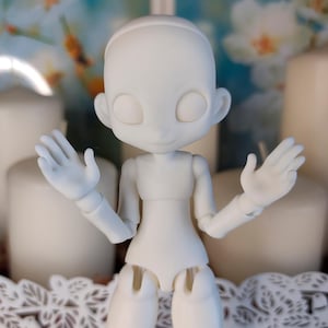 May include: A matte white ball-jointed doll with a smooth, featureless face, large circular eye sockets, and articulated limbs. The doll is posed with both hands raised, palms facing forward, showcasing its modular construction and joints.