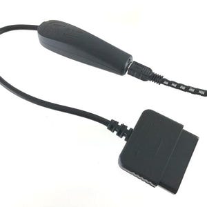 May include: A black electronic adapter cable featuring a rectangular multi-pin connector on one end and a black plastic housing unit on the other. The housing connects to a braided black and white cord via a small port, facilitating data transfer.