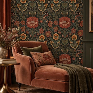 May include: A rust-colored velvet chaise lounge featuring a dark green knit throw blanket, a solid olive green pillow, and a patterned rust-colored pillow. The chaise is positioned against a dark wallpaper with a repeating floral and vine pattern.