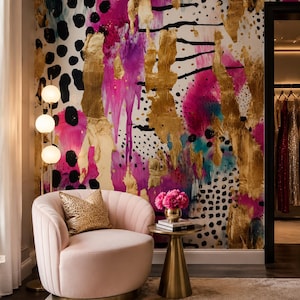 May include: A pale pink channel-tufted armchair with a gold leopard print throw pillow, positioned next to a gold pedestal side table holding a small vase of pink flowers and books, set against a vibrant wall with gold, pink, and black patterns.
