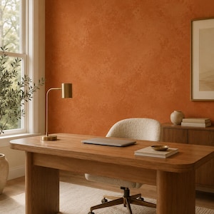 May include: A wooden desk with rounded edges and thick legs, paired with a cream-colored textured swivel chair. On the desk sits a gold-toned metal lamp, a closed laptop, and a small bowl resting on a stack of books.